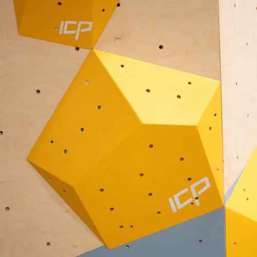 Small yellow ICP Ian I1.2 S climbing volume mounted on a wood-textured wall, designed for precise and technical route setting.