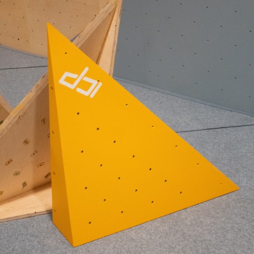 Yellow ICP Johno J1.1 M climbing volume with t-nuts, stacked on safety matting, ready for installation on the climbing wall.