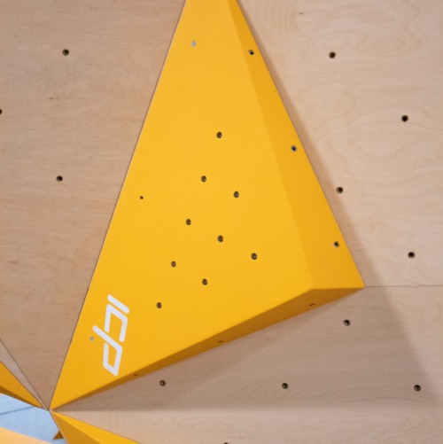Yellow ICP Johno J1.2 S climbing volume with visible t-nuts, mounted on a wood-textured ICP climbing wall.