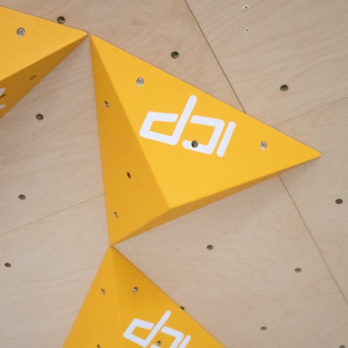 Yellow ICP Kai K1.3 XS climbing volume mounted on a wood-textured climbing wall, viewed front-on.