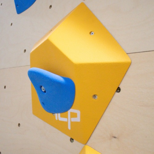 Small yellow ICP Ian I1.3 XS climbing volume on a wood-textured wall, fitted with a blue climbing hold for added route complexity.