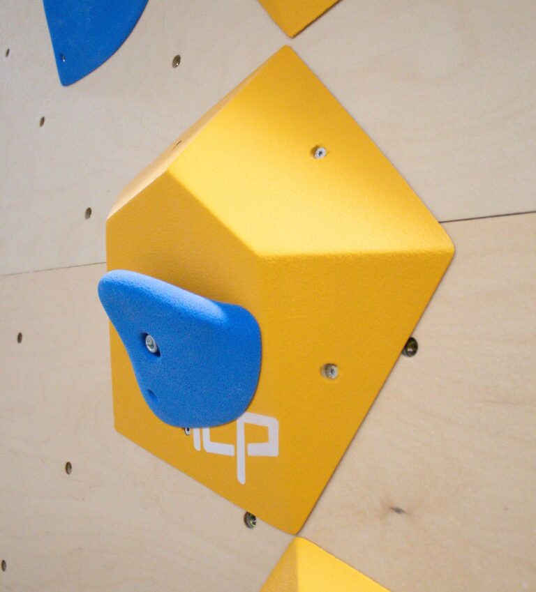 Small yellow ICP Ian I1.3 XS climbing volume on a wood-textured wall, fitted with a blue climbing hold for added route complexity.