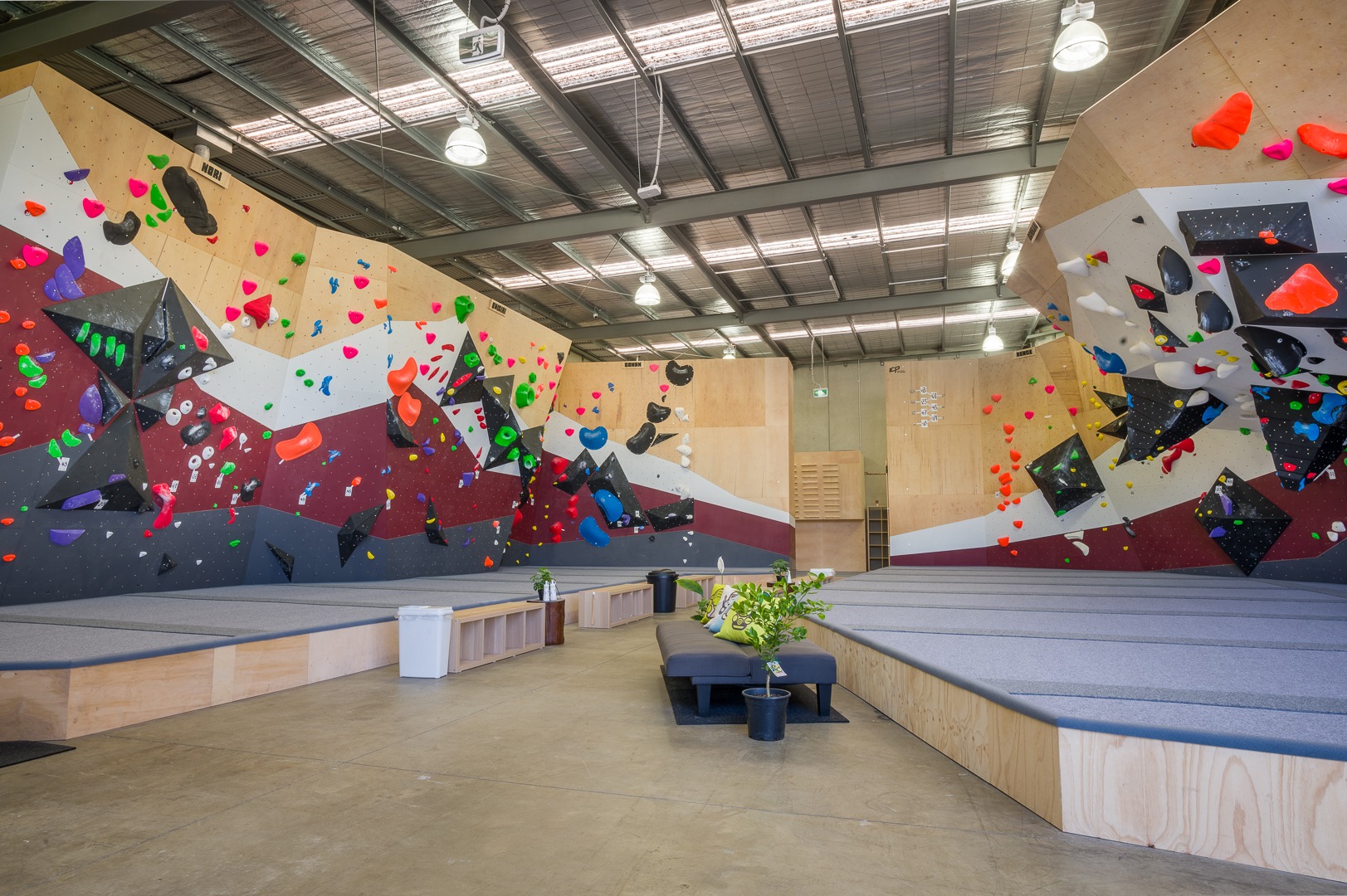 A bouldering gym with white, red and black paint work built by international climbing wall builder, ICP. The walls are filled with various colourful holds and volumes.