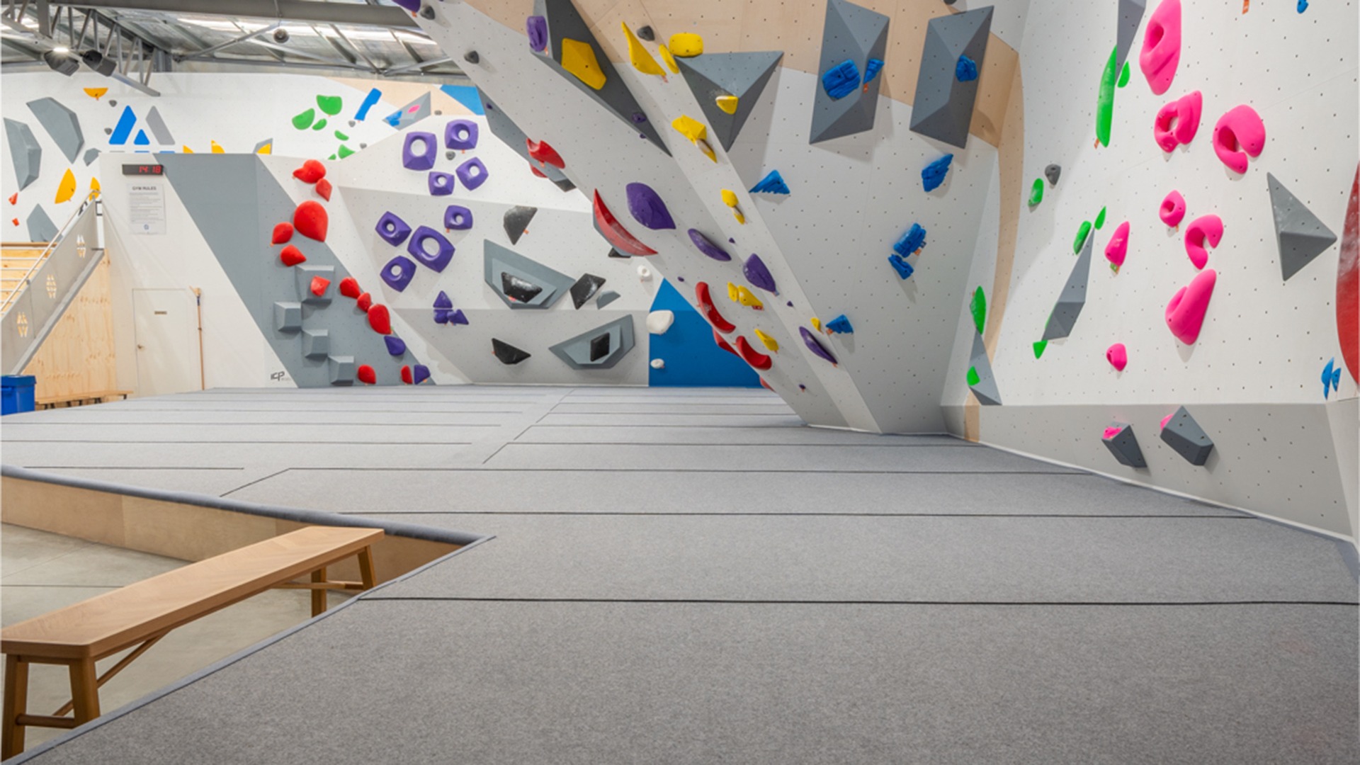 A bouldering gym with a colourful climbing wall and grey carpet climbing mats