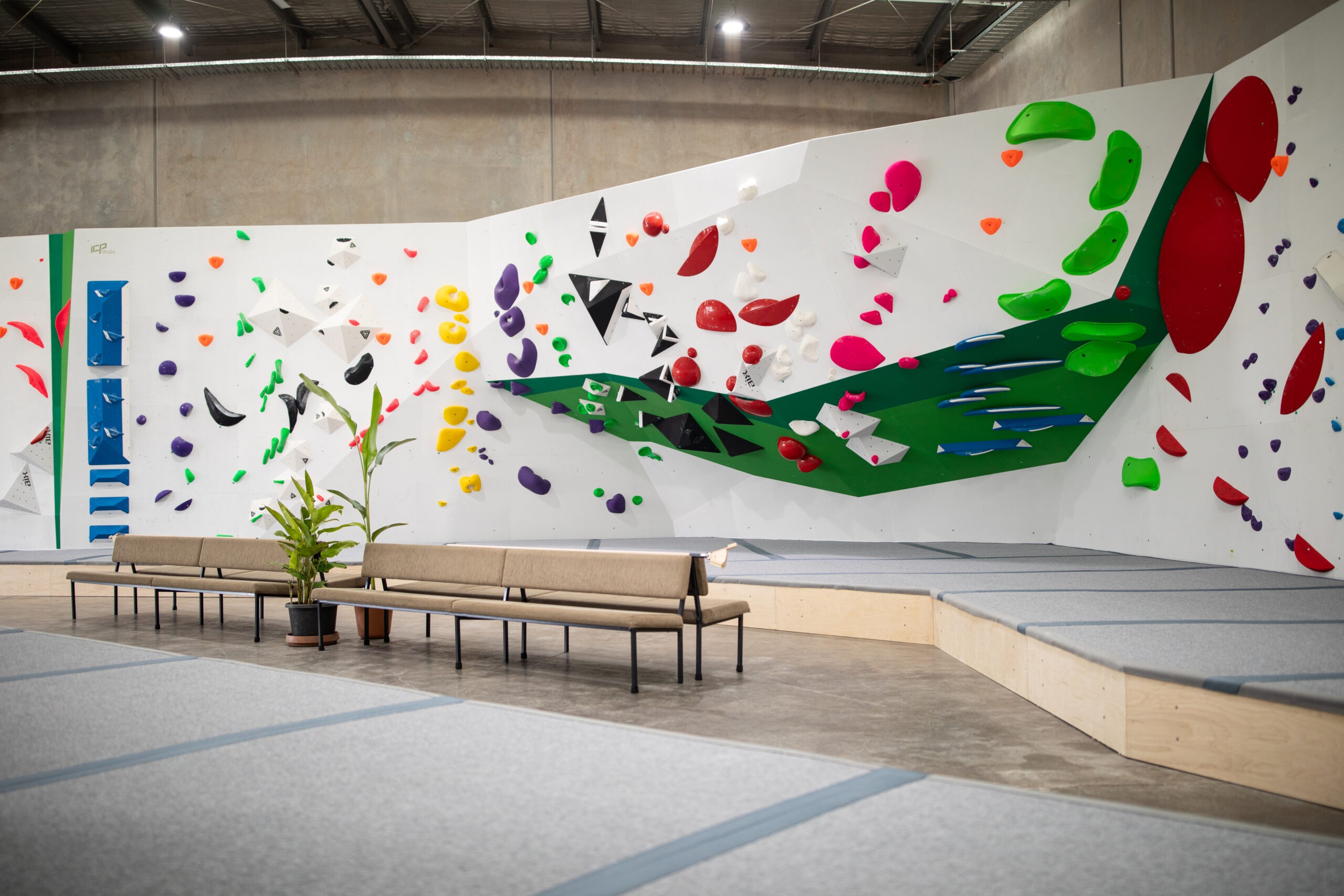 The bouldering mats installed by ICP are covered by grey carpet and dark grey connectors. The Mats are also surrounded by a stylish white and green climbing wall filled with colourful climbing routes and holds. 