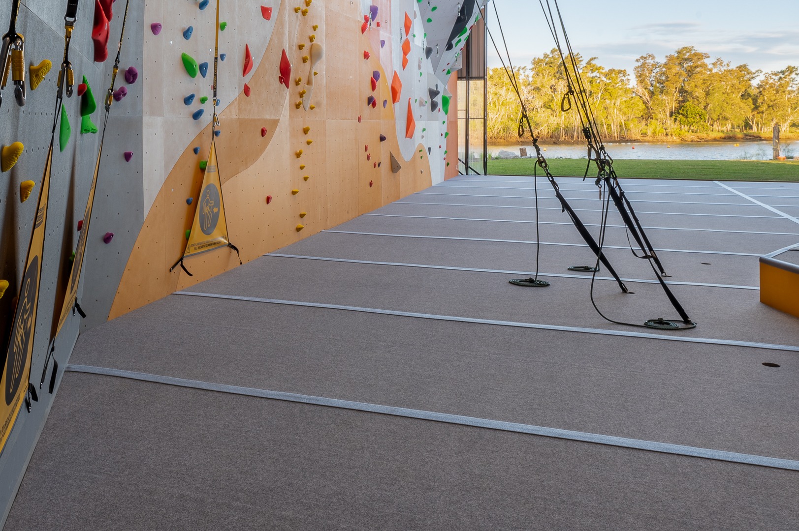 Seamless rope climbing mats installed under a orange climbing walls. The climbin gym is built next to a beautiful river and green backdrop. 