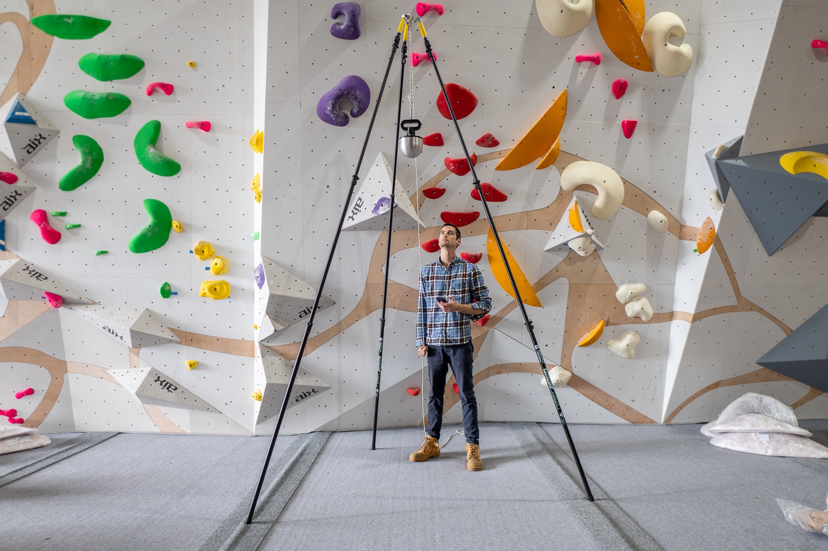 An engineer testing the safety of ICP mats using a measuring equipment. The climbing mats are grey and surrounded by a colourful ICP climbing wall. 
