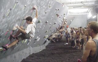A old school climbing wall in a gym with black tired rubber matting.