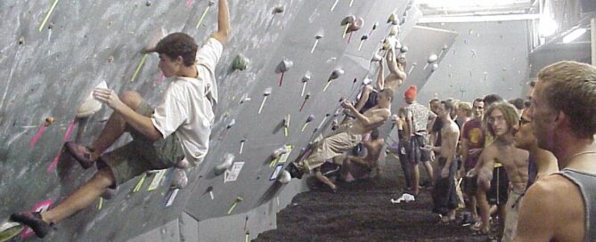 A old school climbing wall in a gym with black tired rubber matting.