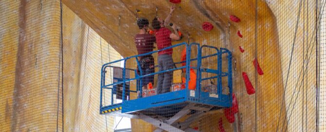 Two people setting a leading climbing wall using a scissor lift machine.