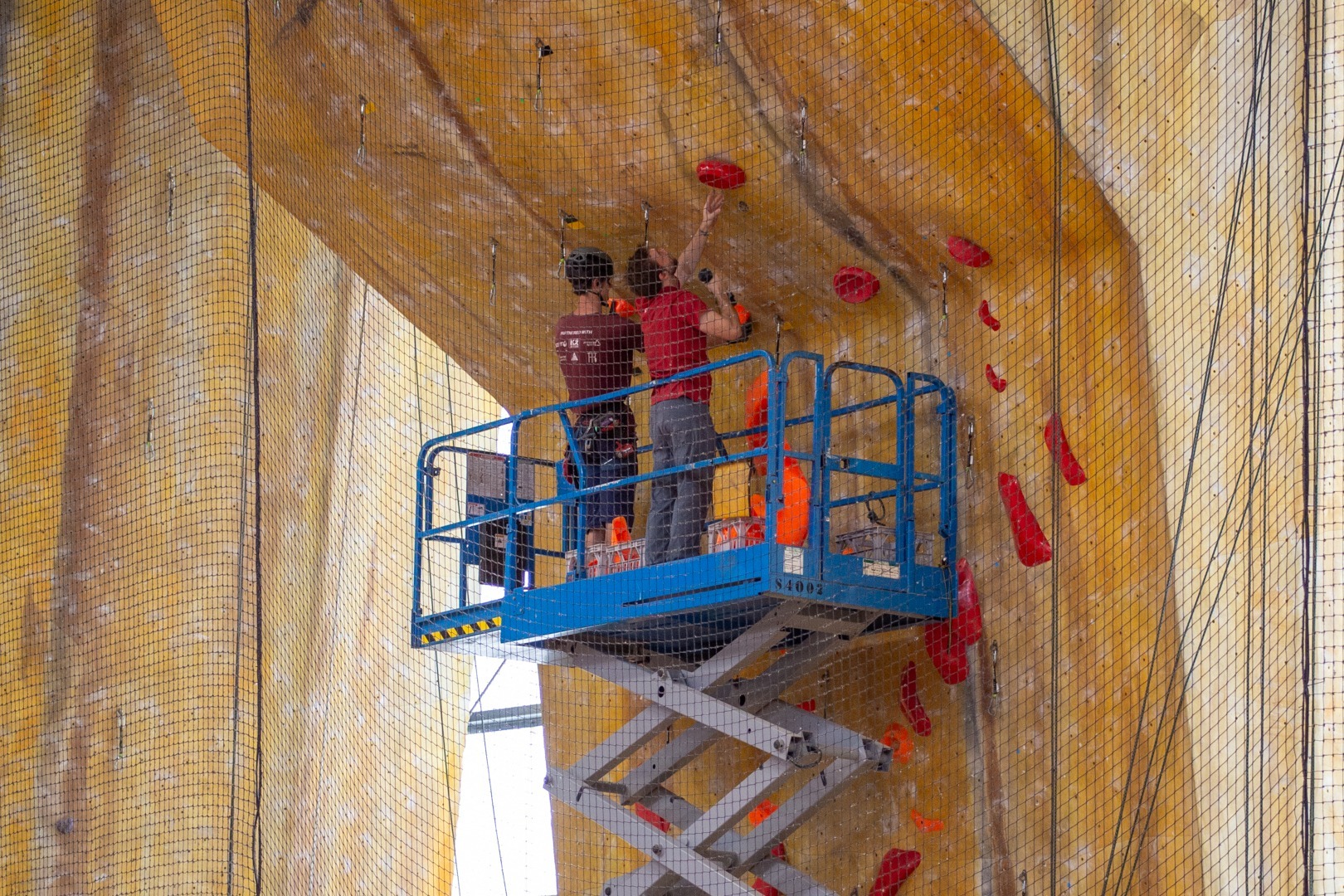 Two people setting a leading climbing wall using a scissor lift machine.