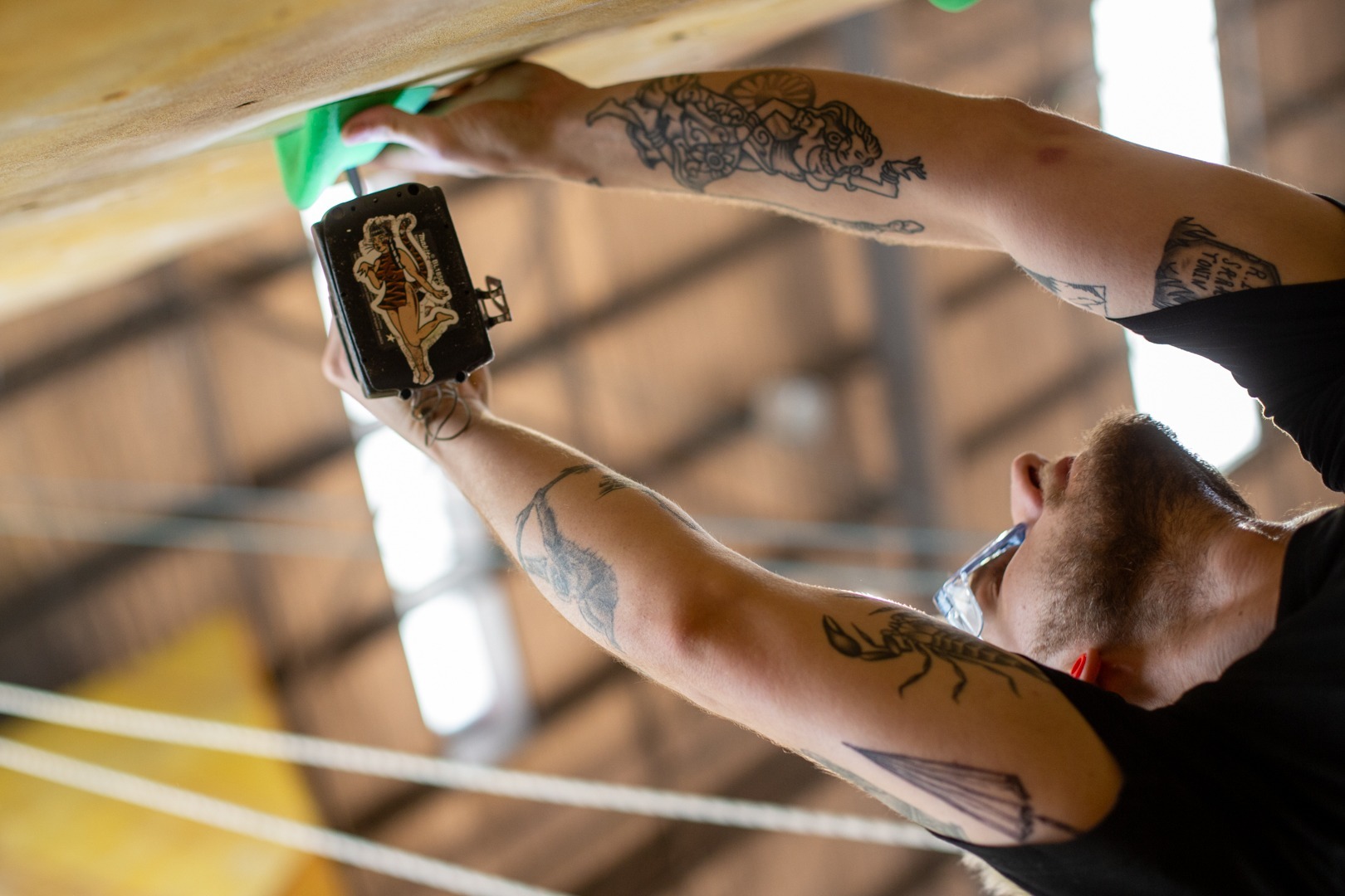 A man with tattoos climbing on a wall.