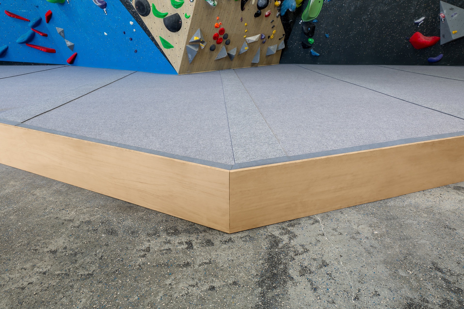 Climb ICP's signature grey carpeted climbing mats surrounded by a high quality timber trim. The mats are located below a colourful climbing wall. 