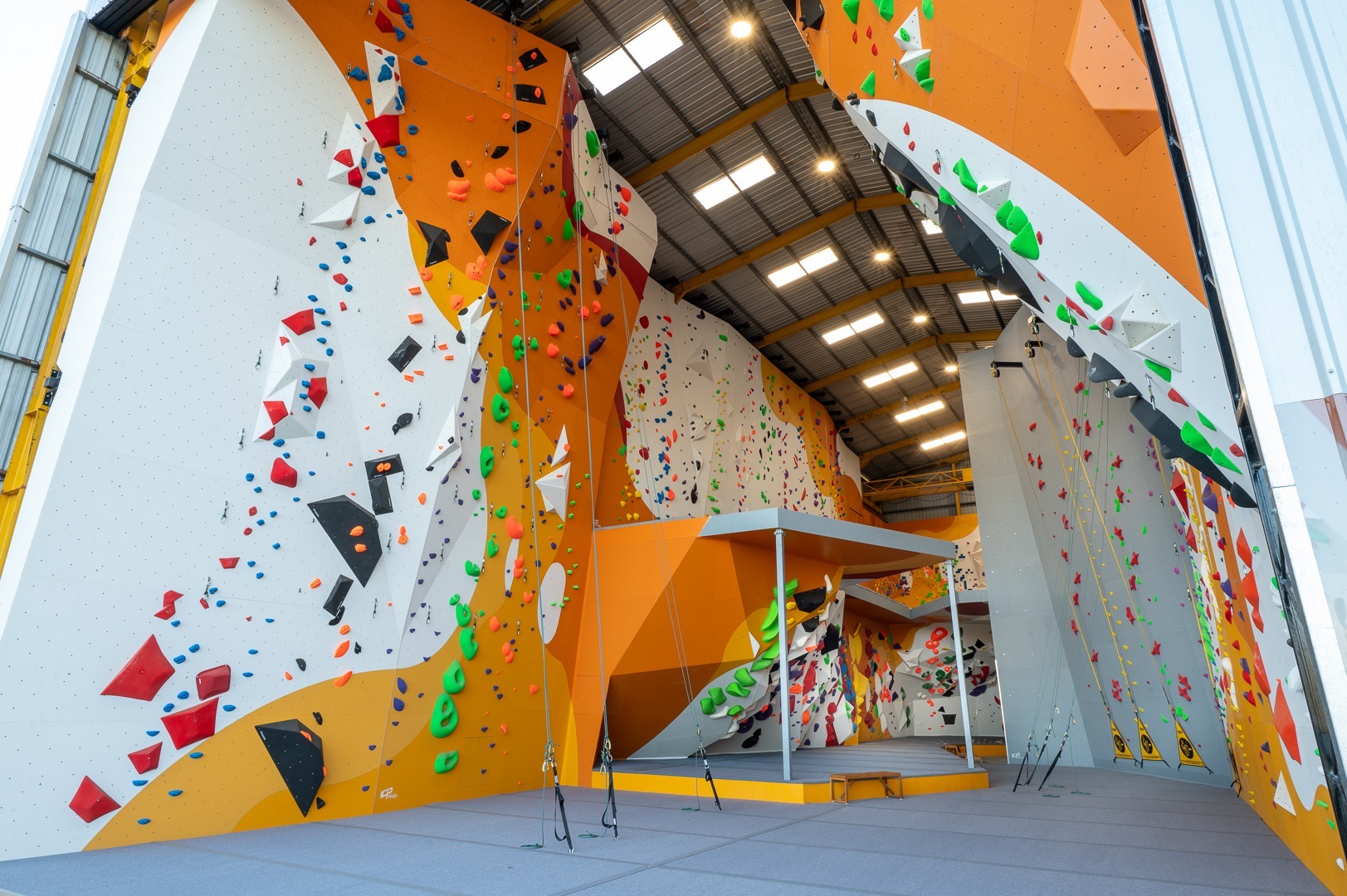 A bouldering gym with white, red and black paint work built by international climbing wall builder, ICP. The walls are filled with various colourful holds and volumes.