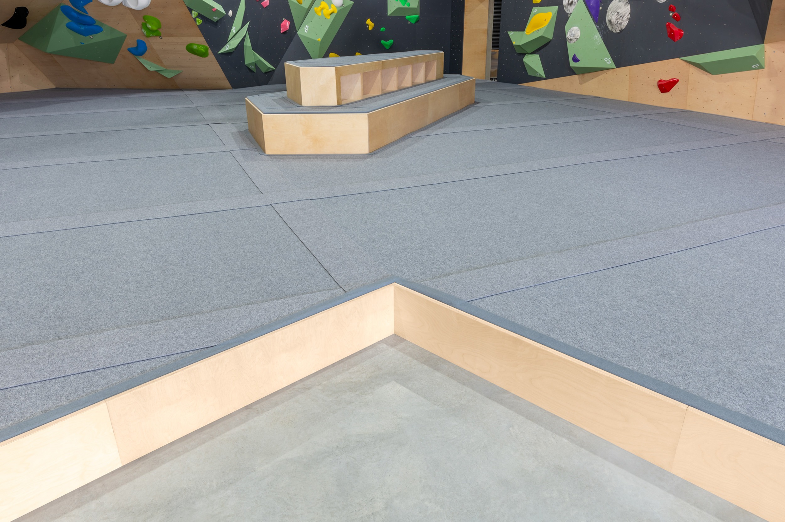 Climb ICP's signature grey carpeted climbing mats surrounded by a high quality timber trim. The mats are located below a colourful climbing wall. 