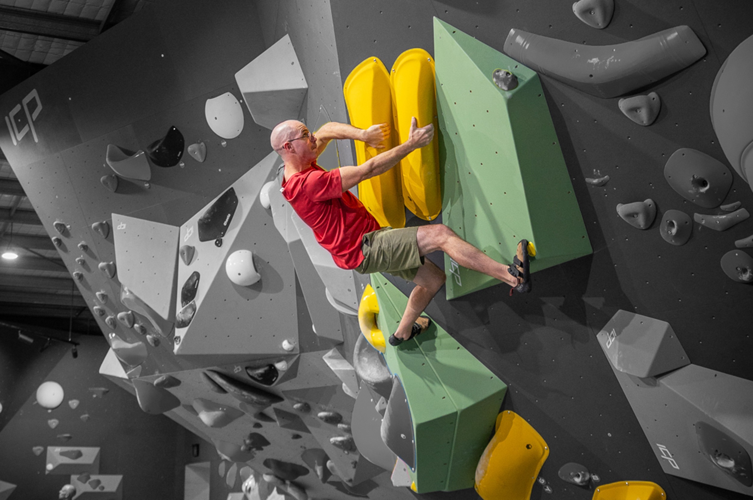 A route setter placing a black hold cross a wooden ICP volume and a climbing wall at ICP Boulderhall & Showroom. The climbing wall is tall and white, which also has a unique wooden detail across the bottom. 