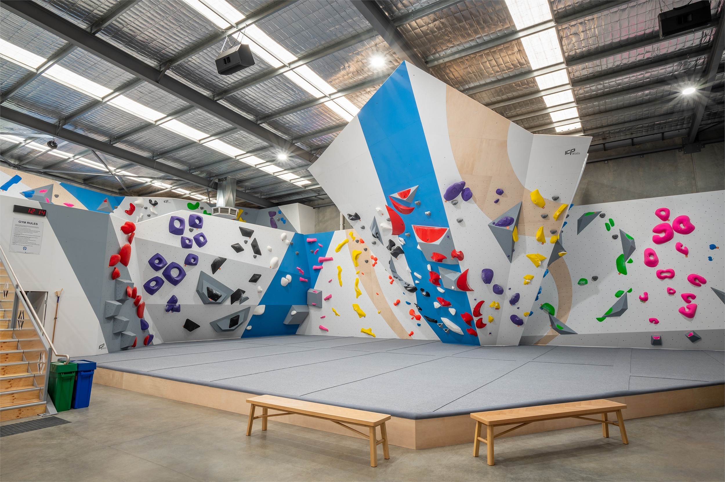 The bouldering mats installed by ICP are covered by grey carpet and dark grey connectors. The Mats are also surrounded by a stylish white and green climbing wall filled with colourful climbing routes and holds. 