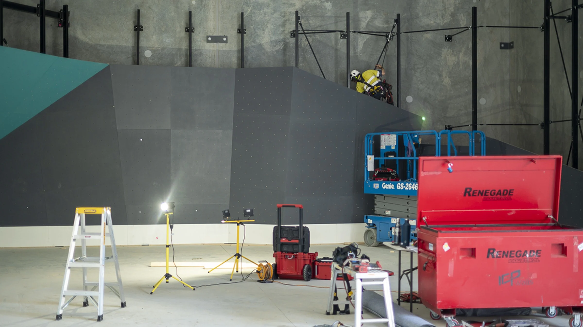 ICP Climbing Wall Installation – Modern Indoor Gym Construction ICP climbing wall builders installing a modern indoor climbing gym with tools and lift equipment.