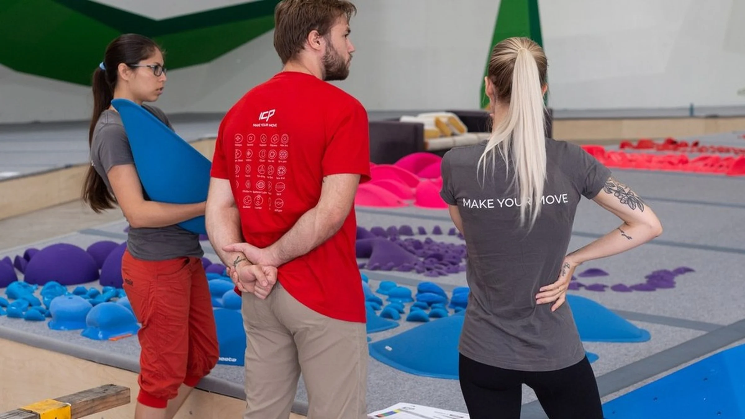 Three ICP routesetters stand in discussion beside holds on the bouldering mats inside and ICP built indoor climbing gym.