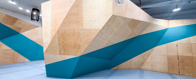Indoor geometric plywood sculpture with beige panels and teal-blue accents in a bright, modern space.