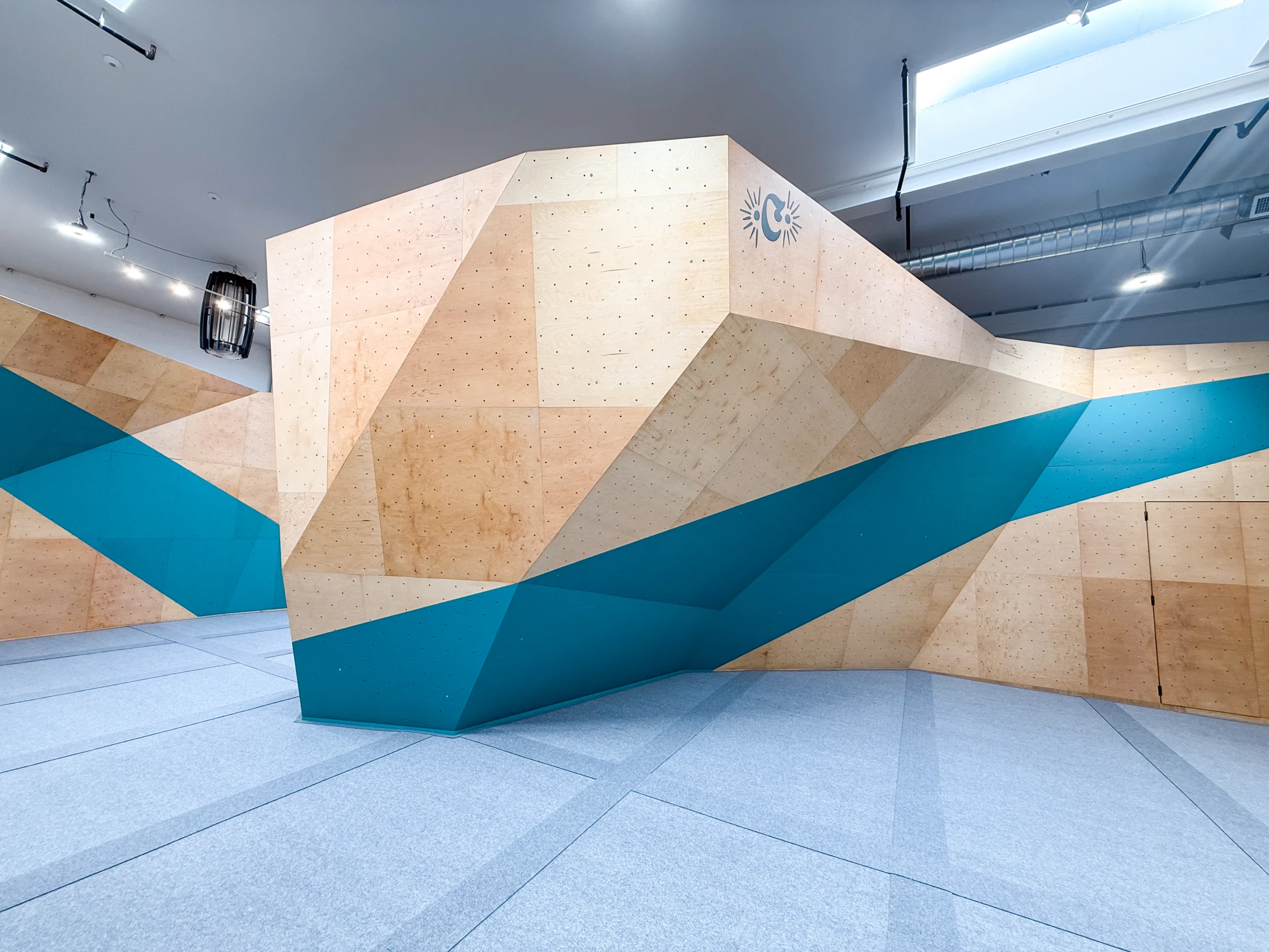 Indoor geometric plywood sculpture with beige panels and teal-blue accents in a bright, modern space.
