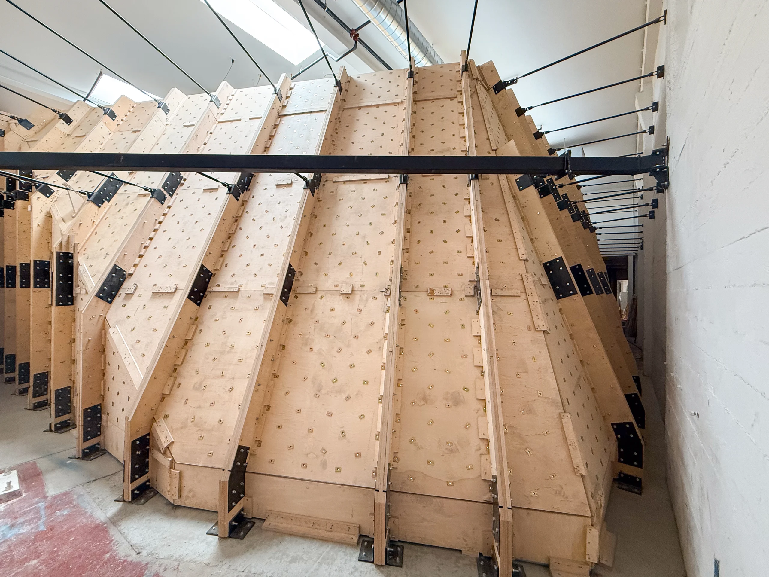 Large wooden concrete formwork panels curved into a wall, strapped with metal plates and bolts in an industrial space