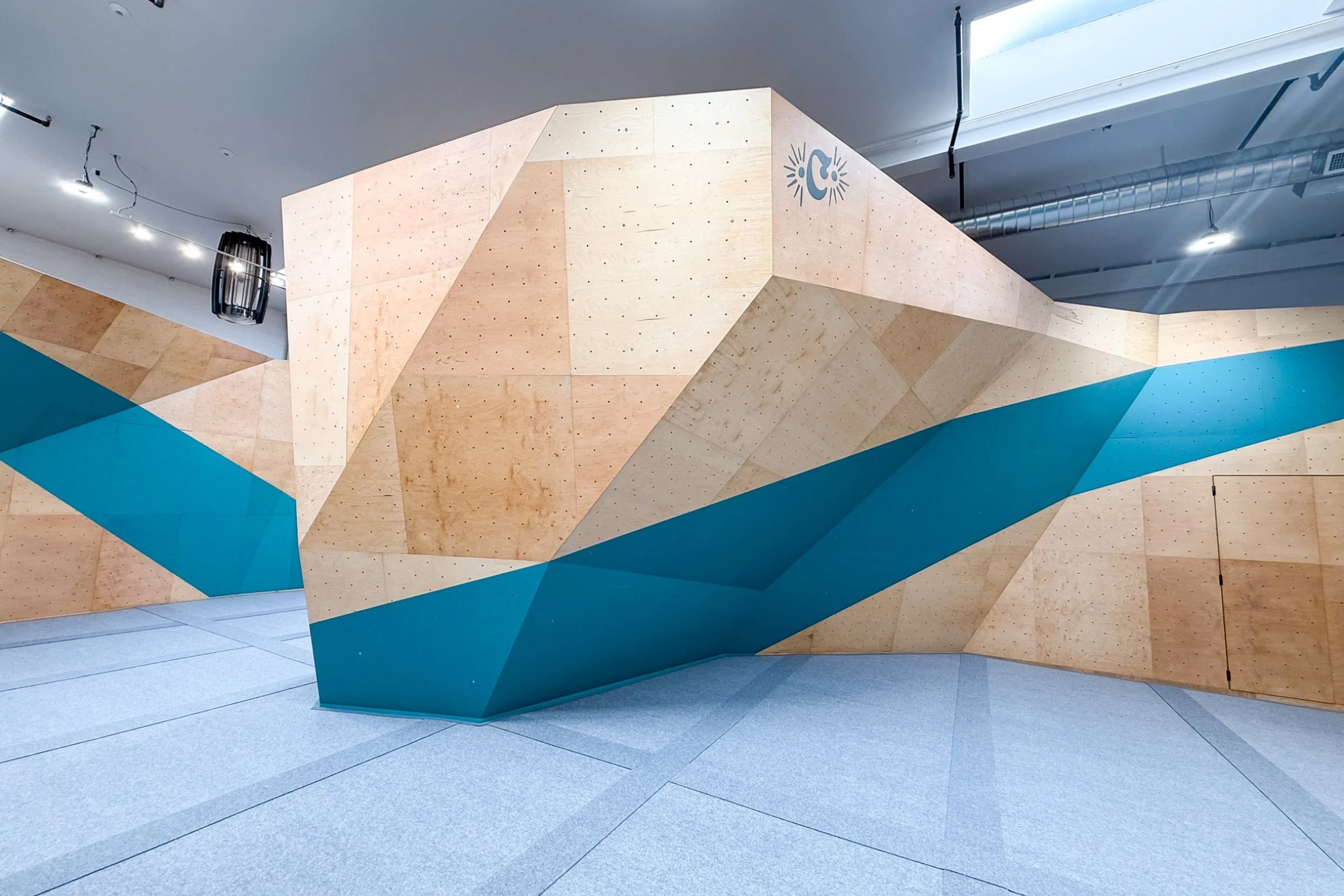 ICP bouldering wall at the California Climbing Collective climbing gym featuring custom geometric wood and painted panel finishes with industry-standard carpet-bonded foam safety matting.